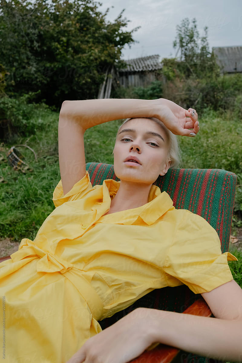 portrait of a stylish girl in a yellow retro dress , which lies in a chair in nature