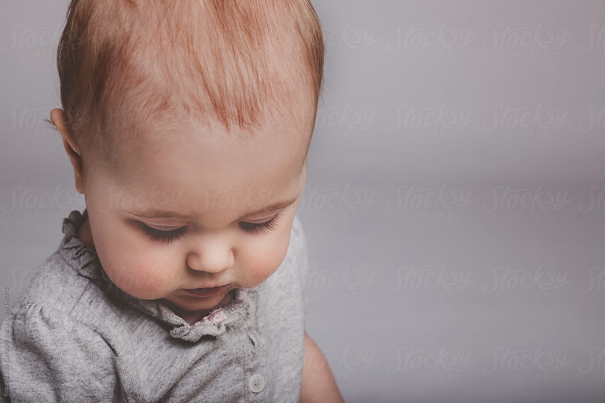 Cute baby girl looking down on solid background
