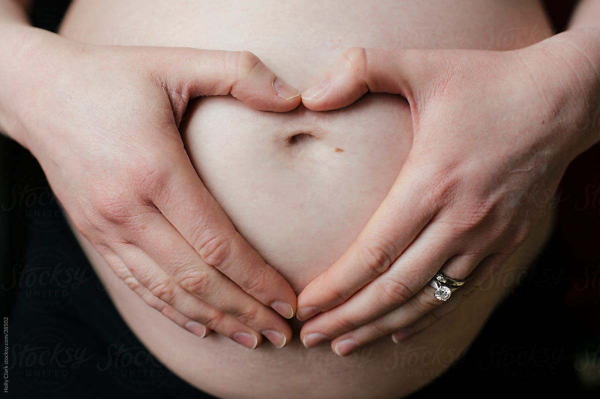 Hands in heart shape on pregnant mother\'s belly