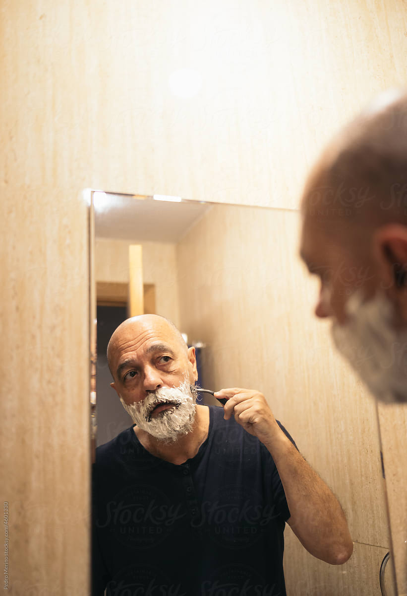 A man shaving his beard in front of the mirror
