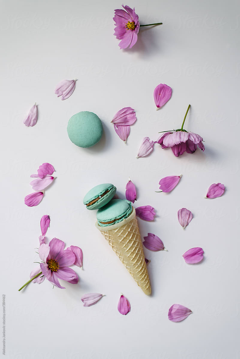 Turquoise macaroons in cone with pink flowers on white background