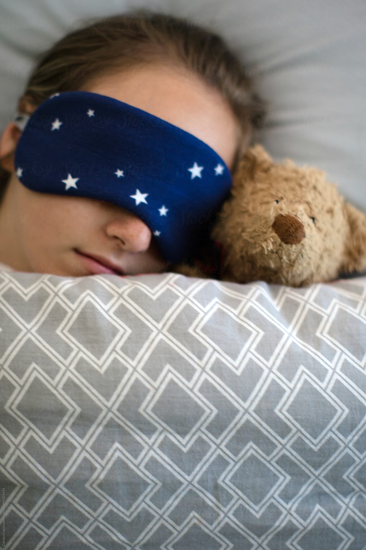 Teenage girl sleeping in bed with her teddy bear and a sleep mask with stars