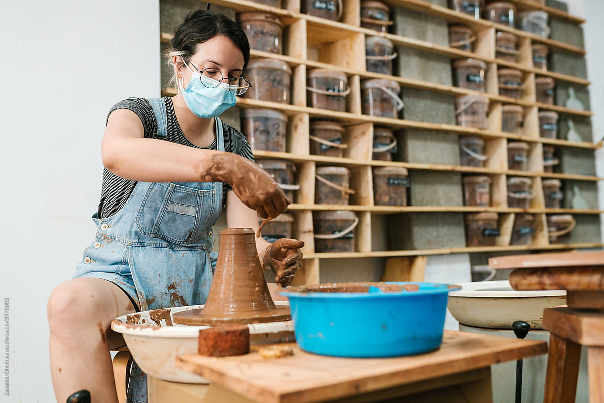 Craftswoman in mask spilling water on clay vase