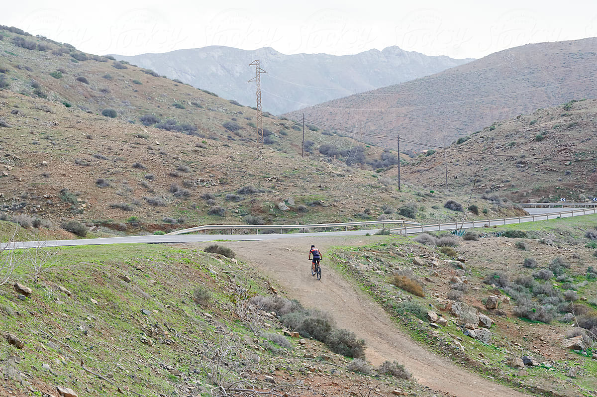 Man mountain biking onto a road from a trail