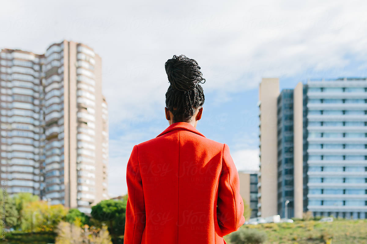 Back view of calm black woman in red jacket looking at city