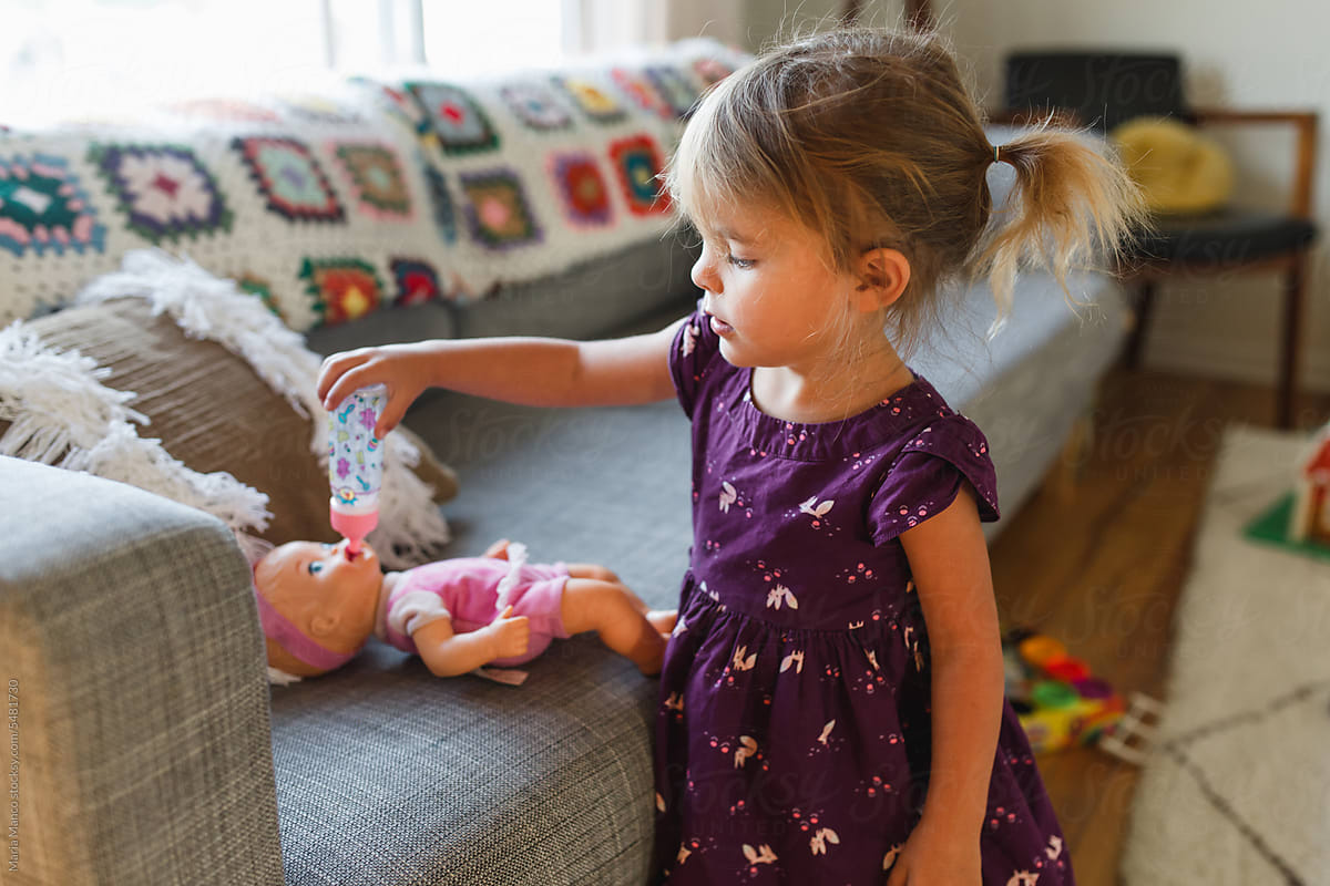 Young girl feeds doll with toy bottle