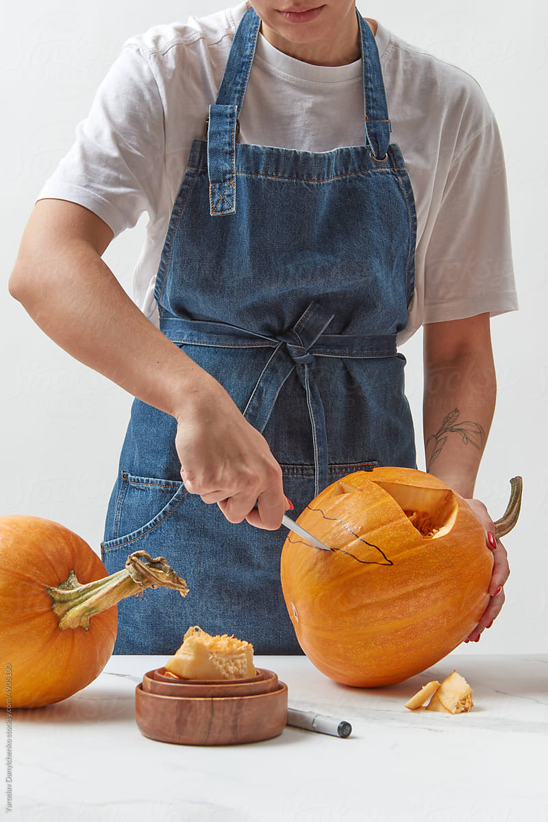 Woman preparing Halloween pumpkin on white table.
