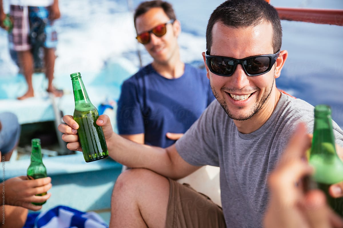 Young man smiling gathering with his friends and having some beers during a boat trip in the sea