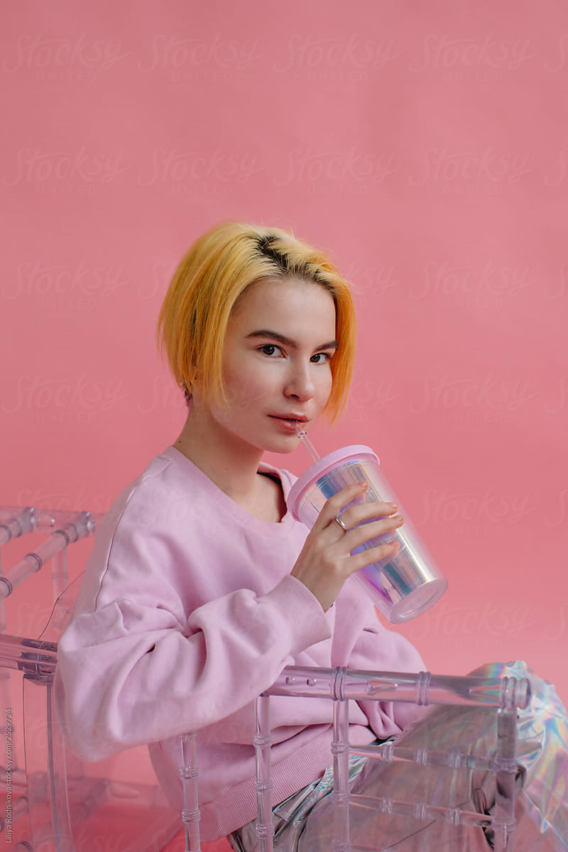 `teenager with yellow hair and  holographic cup on pink background