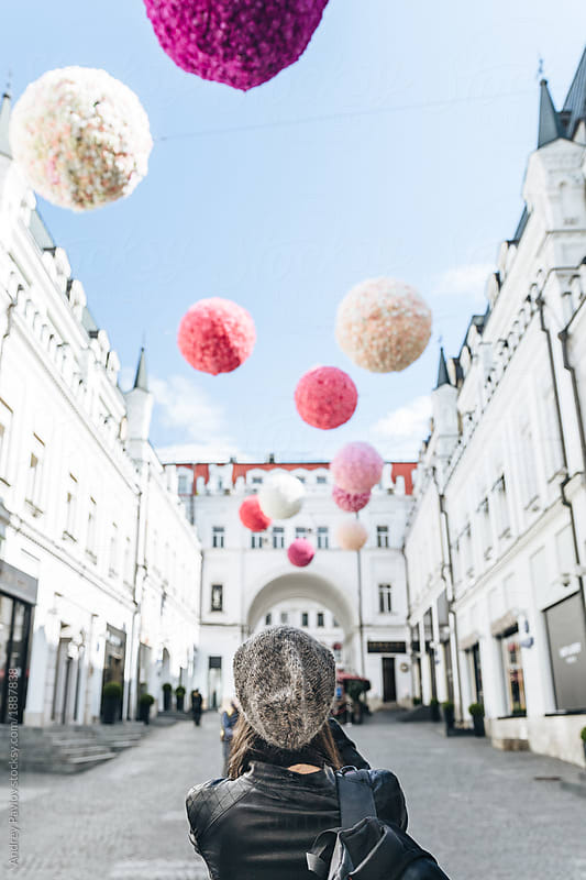 A woman looking at floating pink ball street decorations surrounded by white buildings. Andrey Pavlov for Stocksy United