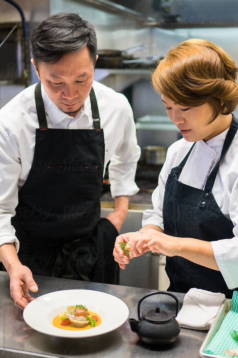 Two Chefs Look Over A Dish Together As They Prep It