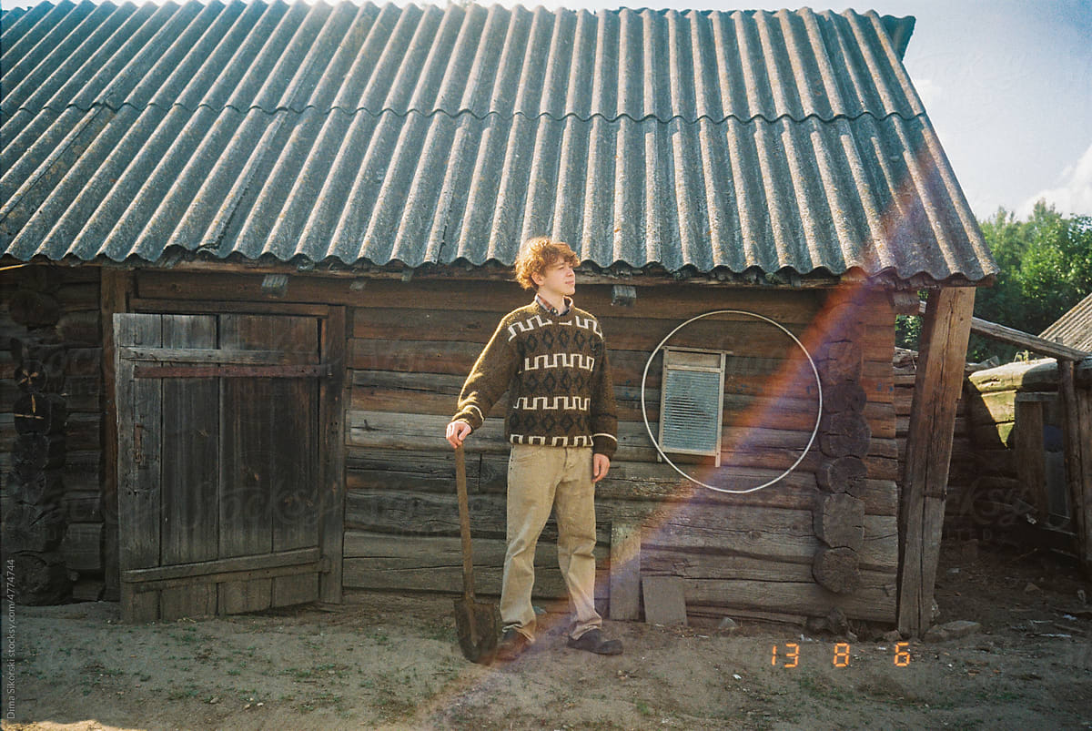 Curly-haired rustic red-haired guy stands with a shovel on the farm