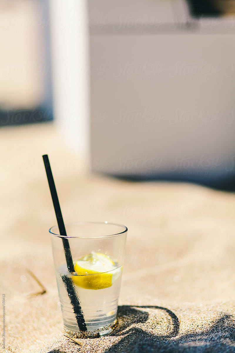 Summer cocktail - tonic and lemon with black straw in the sand