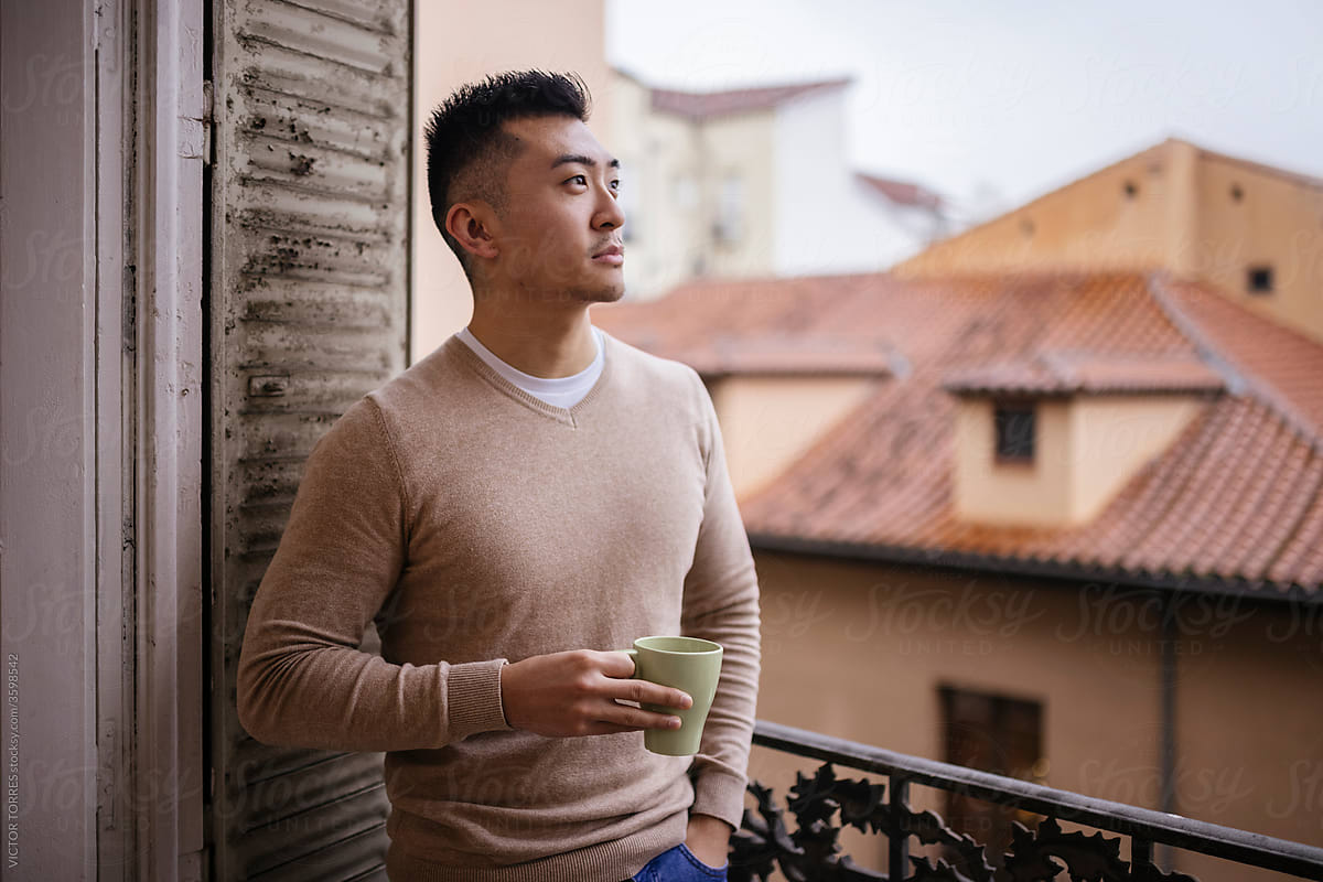 Cheerful Asian man with a cup of coffee on balcony