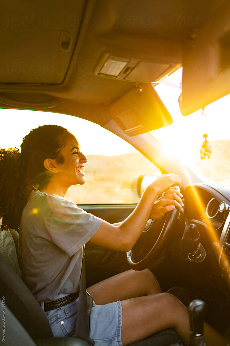 Pretty woman smiling while she is driving a car. sunset light flashing
