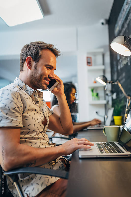 Happy Man Working on Laptop at the Office while Talking on Phone&#xA;
