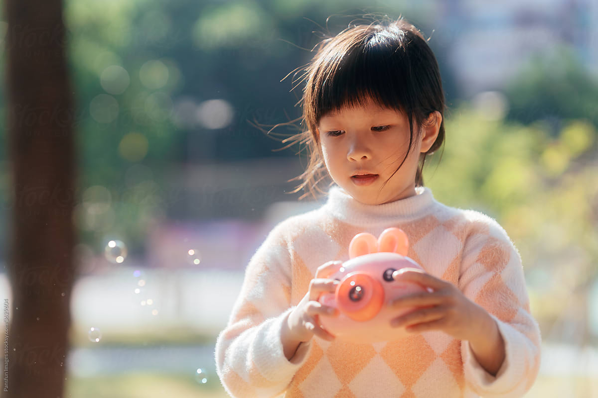Asian little girl playing bubble machine outdoors