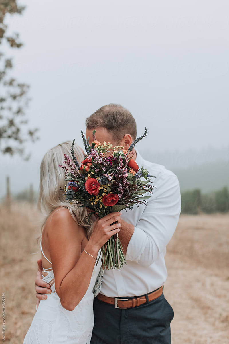 Bride and Groom Kissing behind Bouquet