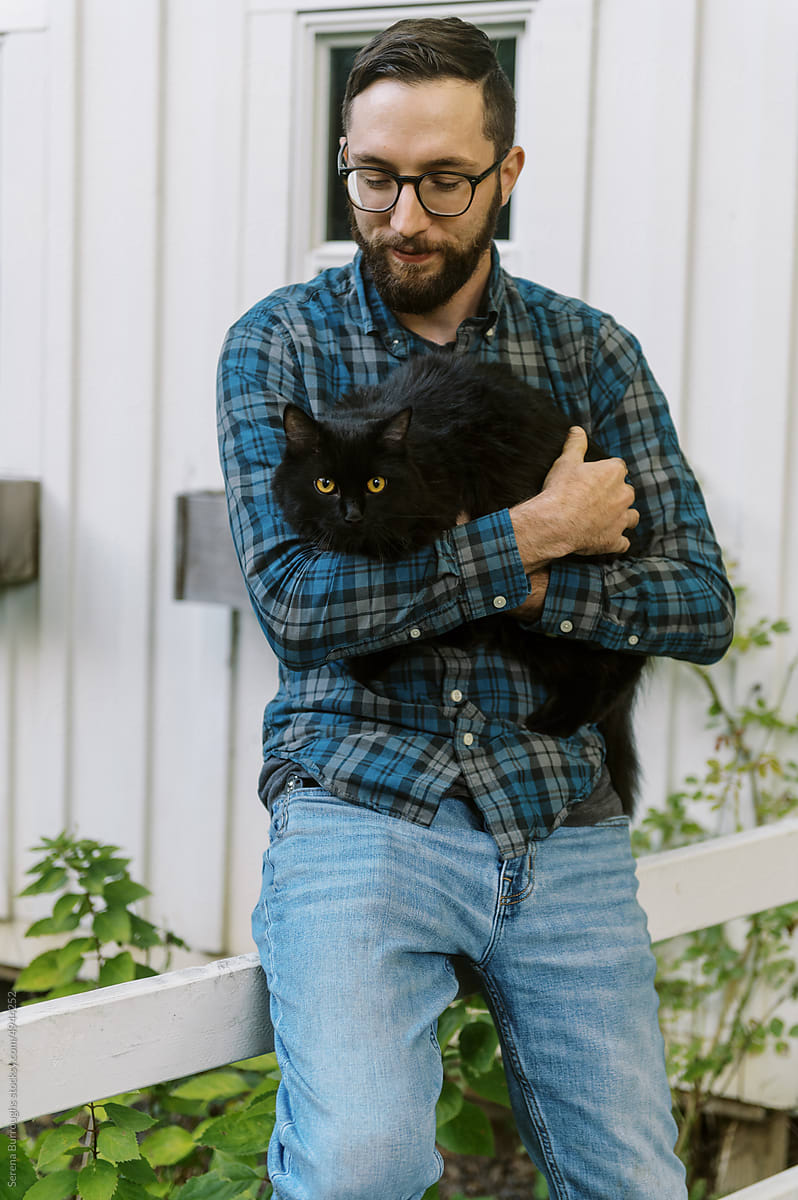 man holding black cat while standing in backyard