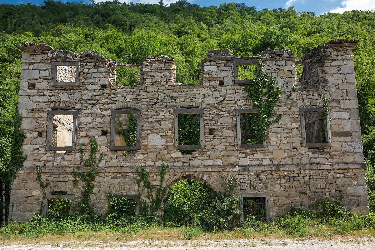 Old stone abandoned house in ruins covered with green leaves