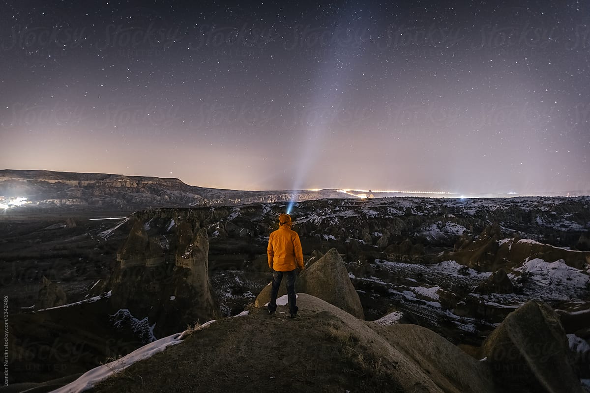 young male adventurer with headlamp overlooking snowcovered landscape of cappadocia at night, turkey