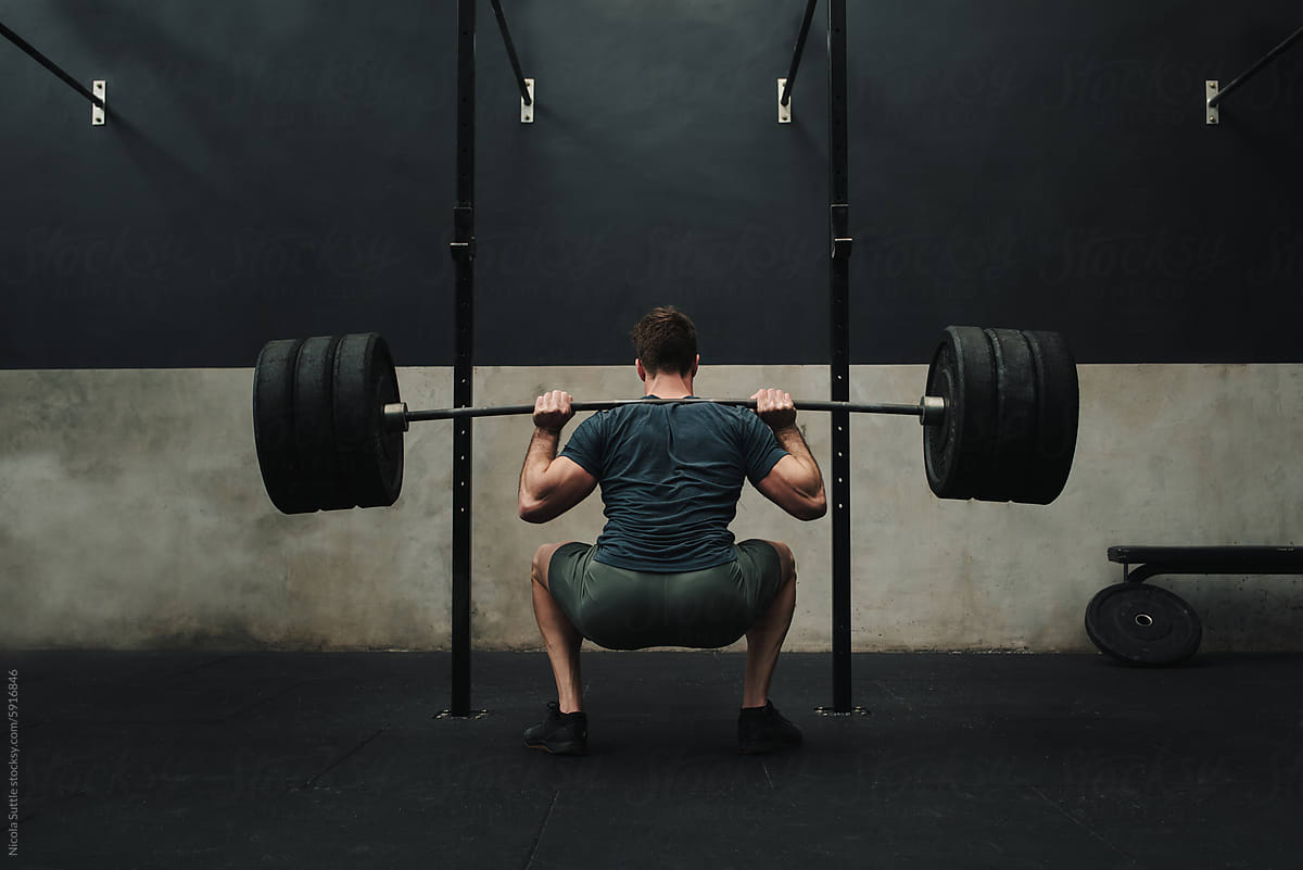 Unrecognizable athlete squatting while lifting barbell behind back