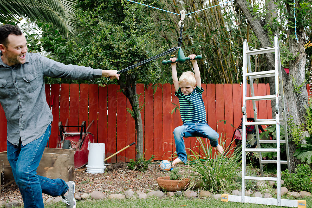 Laughing dad pulling young son on backyard zipline.