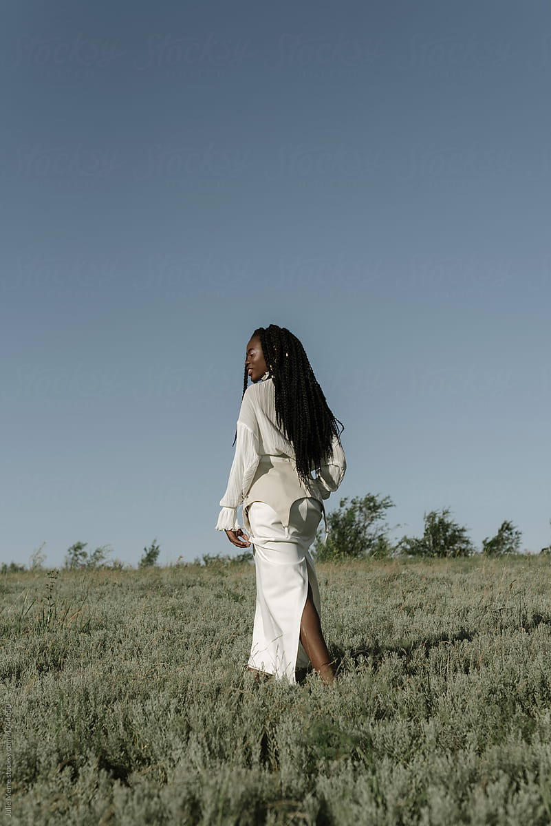 Black woman walking in countryside field in stylish dress
