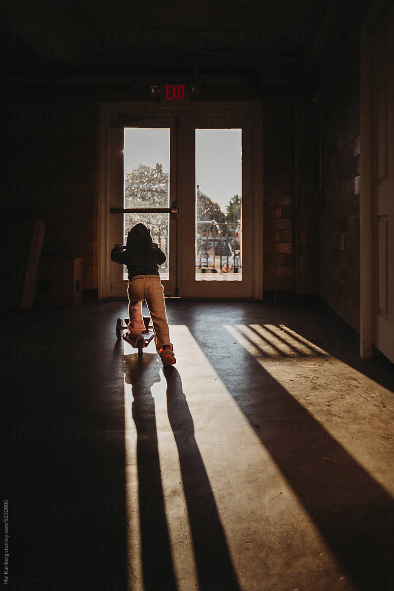 Girl on scooter in dramatic shadow light in front of glass door