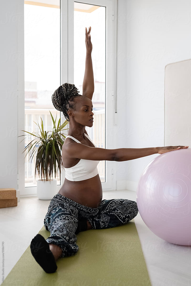 Black pregnant female practicing yoga with birth ball