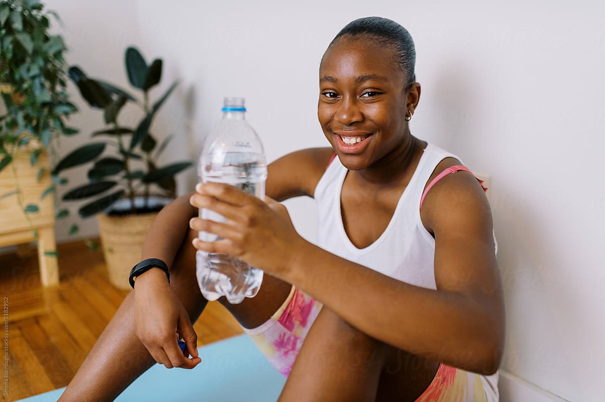 fit black tween girl drinking water from bottle after work out indoors