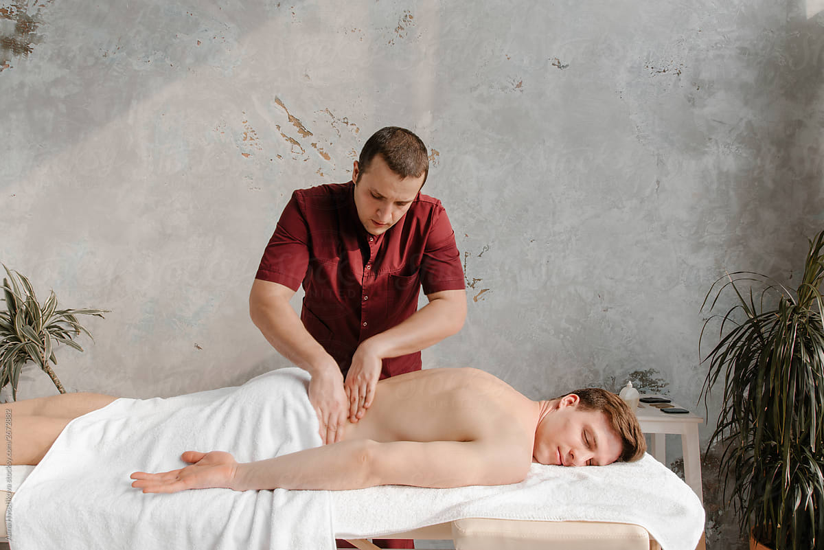 Masseur in red uniform doing massage on loin to man.