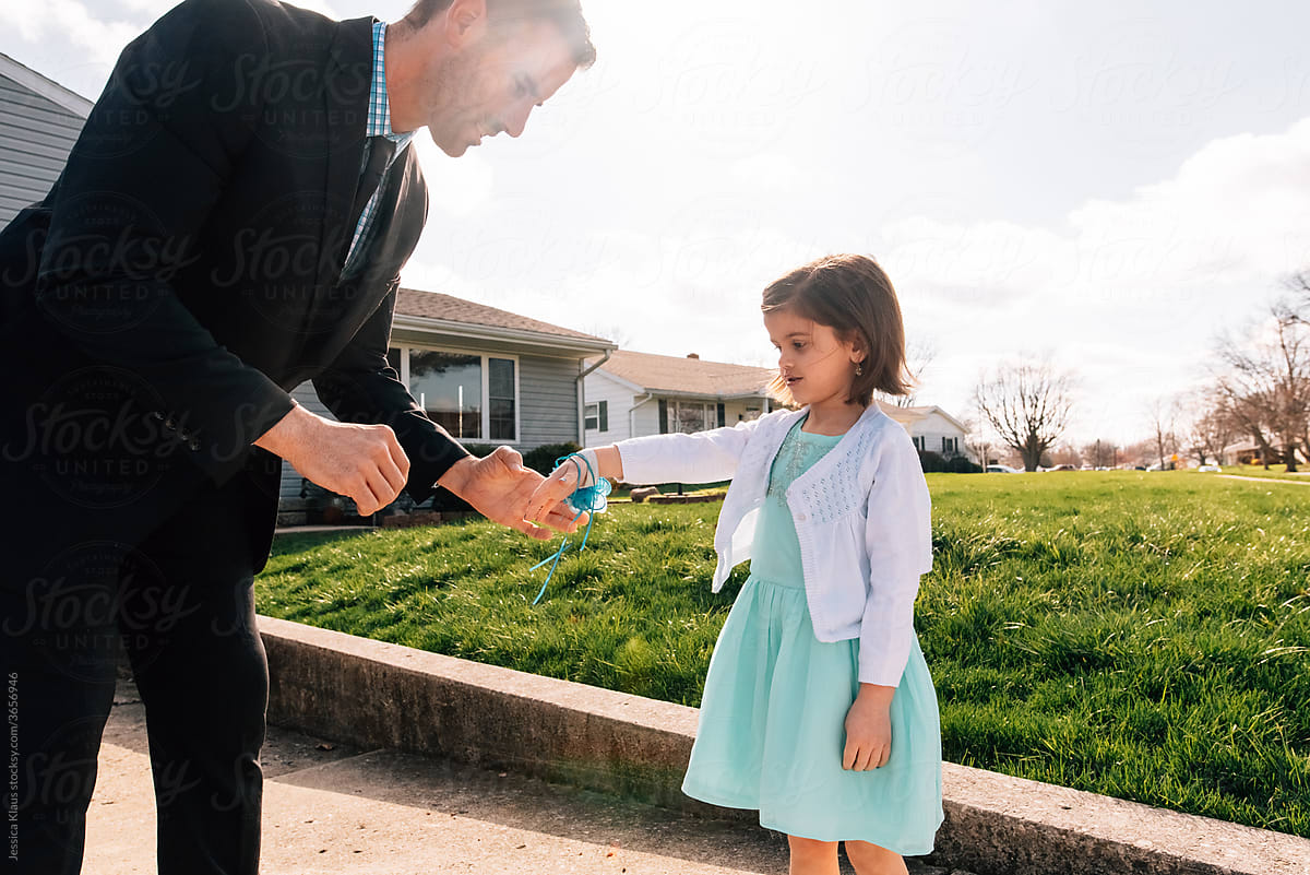 Father putting flower corsage on daughter\'s wrist.