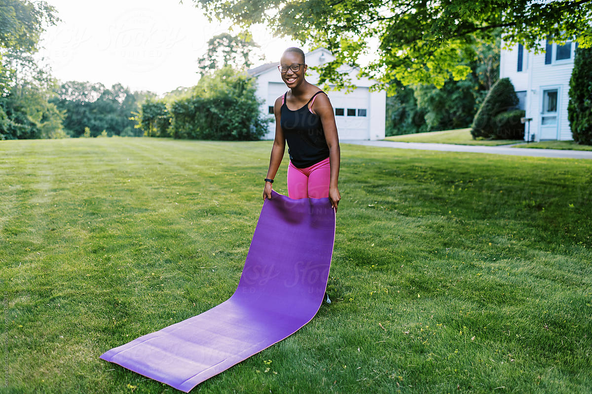 fit black girl with yoga mat outdoors on lawn at sunset