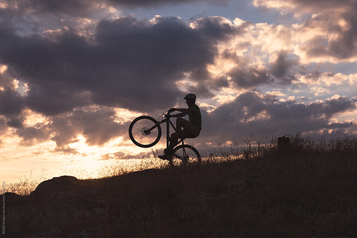 Silhouette doing one wheel on bike beside the sunset sky