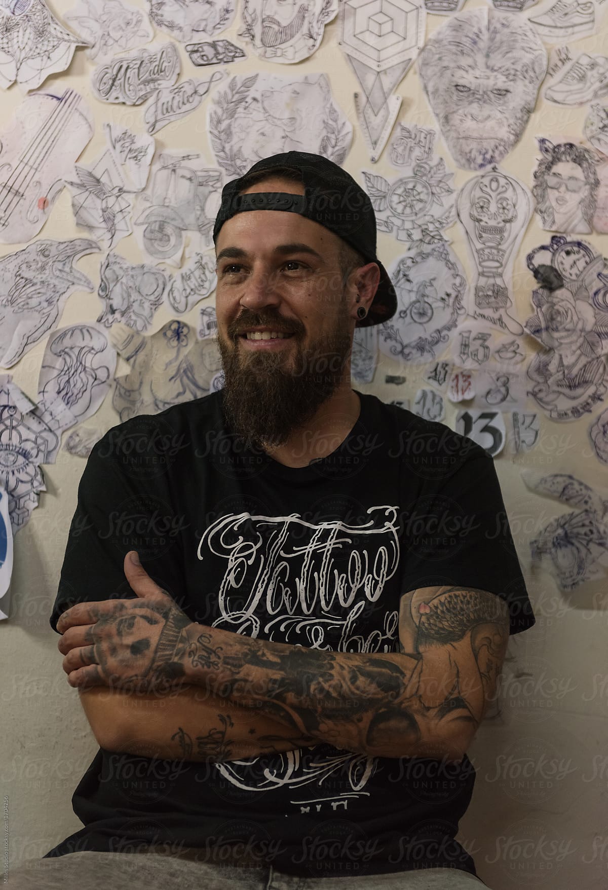 Cheerful man at wall with tattoo sketches