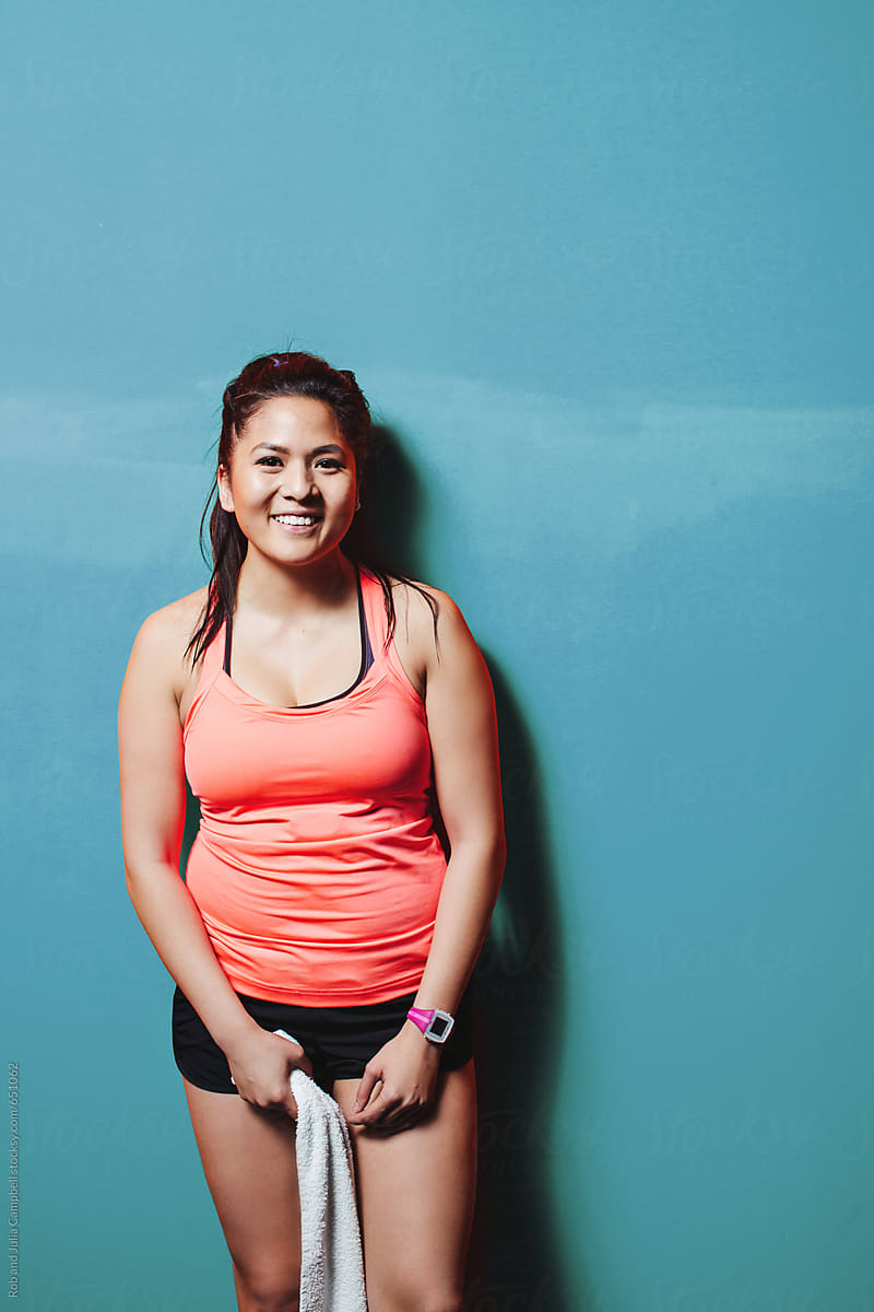 Happy Asian Woman Smiling Near Blue Wall Sweaty And Smiling After Hard Workout By Stocksy