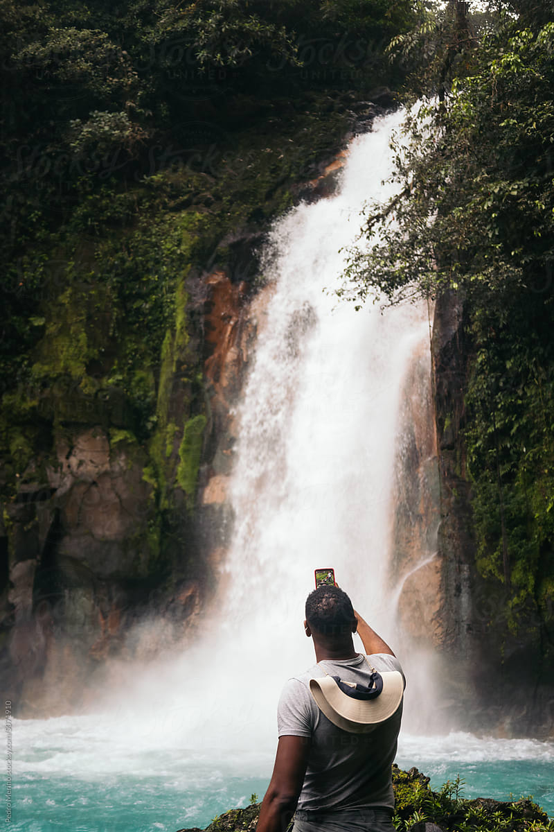 Man visiting the Rio Celeste waterfall in Costa Rica and taking photos