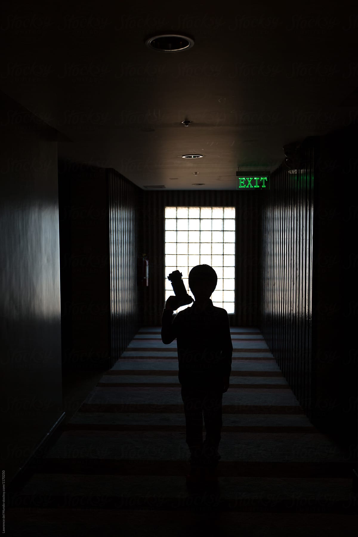 Silhouette of a young boy with a camera, standing in a dark hallway.