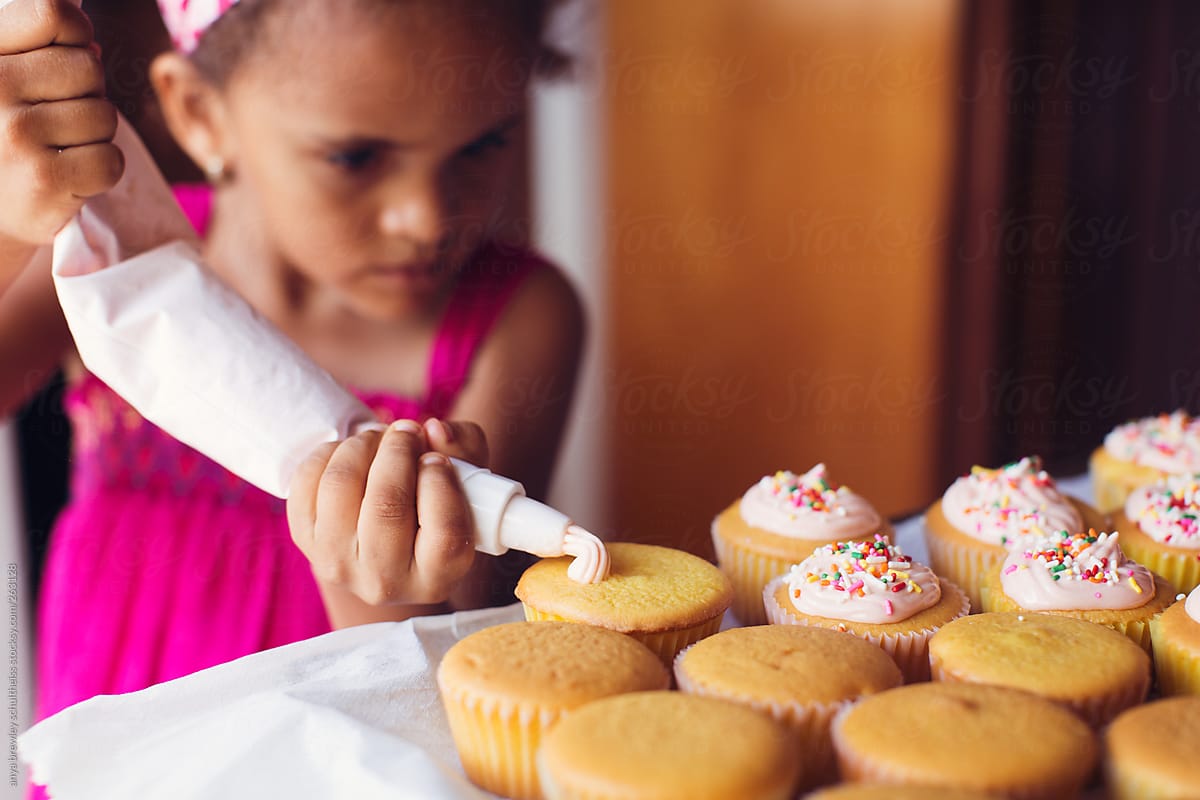 Young girl decorating a batch of cupcakes with icing