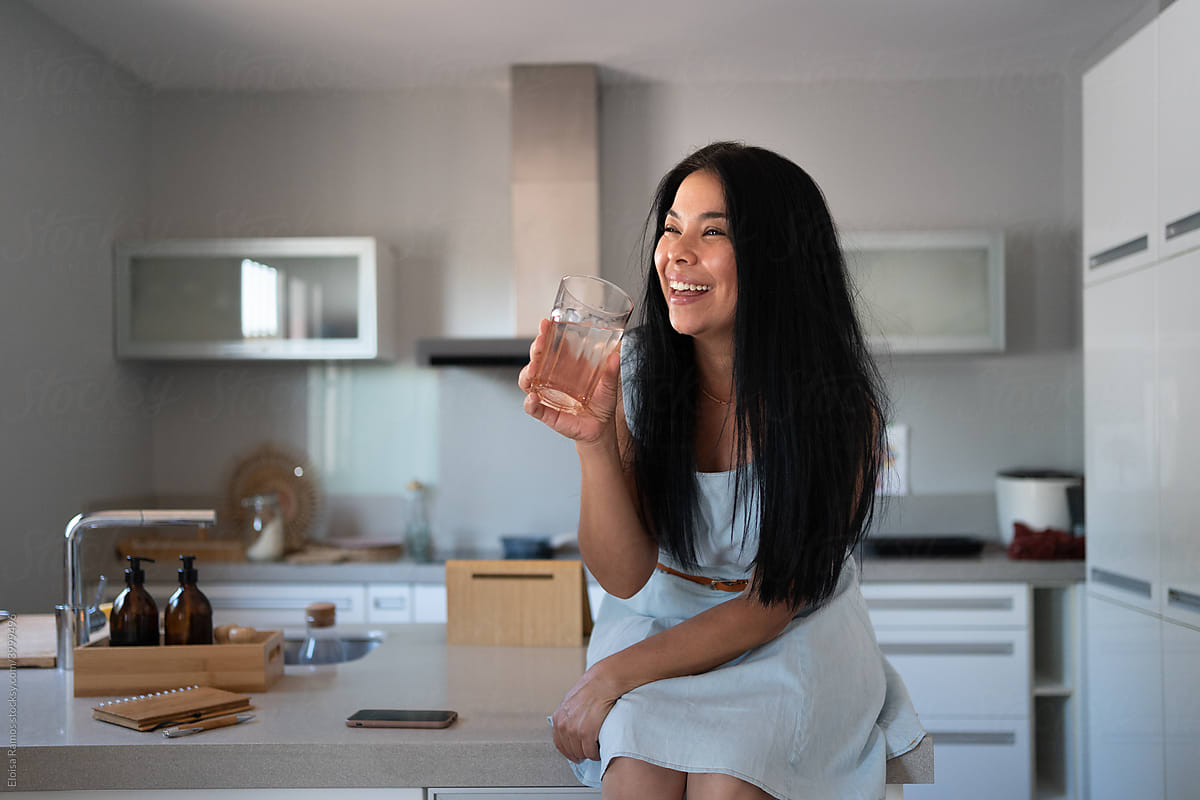 Joyful latin woman drinking water at kitchen