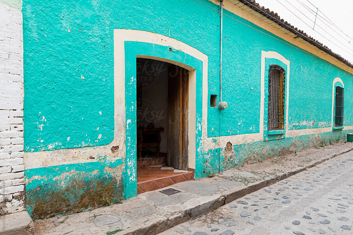 A house painted in aqua color in front of a stone street