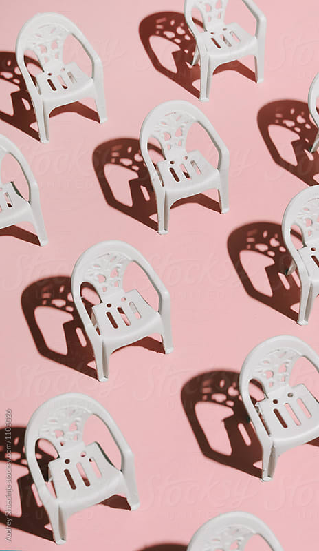 Arranged white chairs in order on pink background.