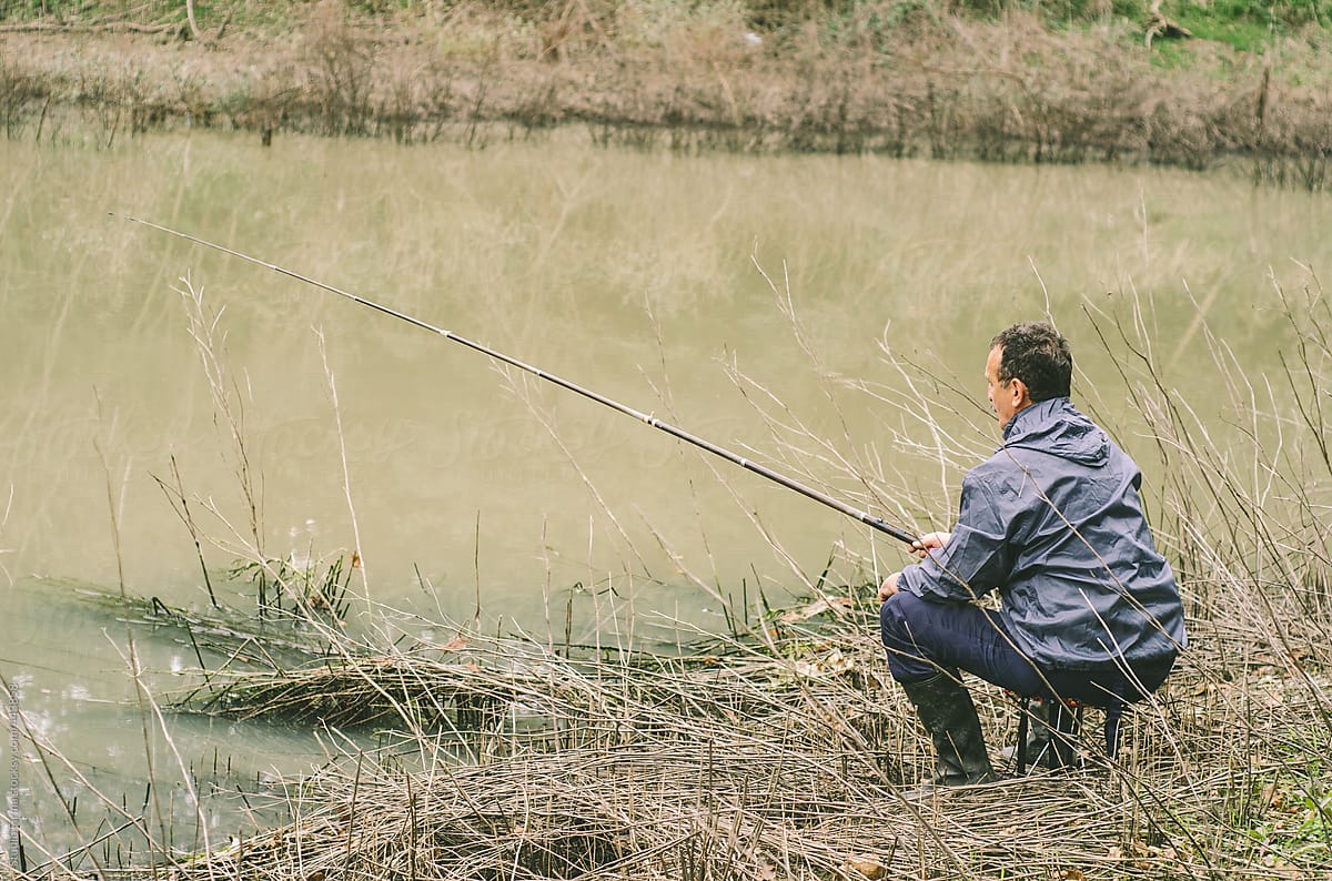 A man at the bank of the river with the fly fishing pole.