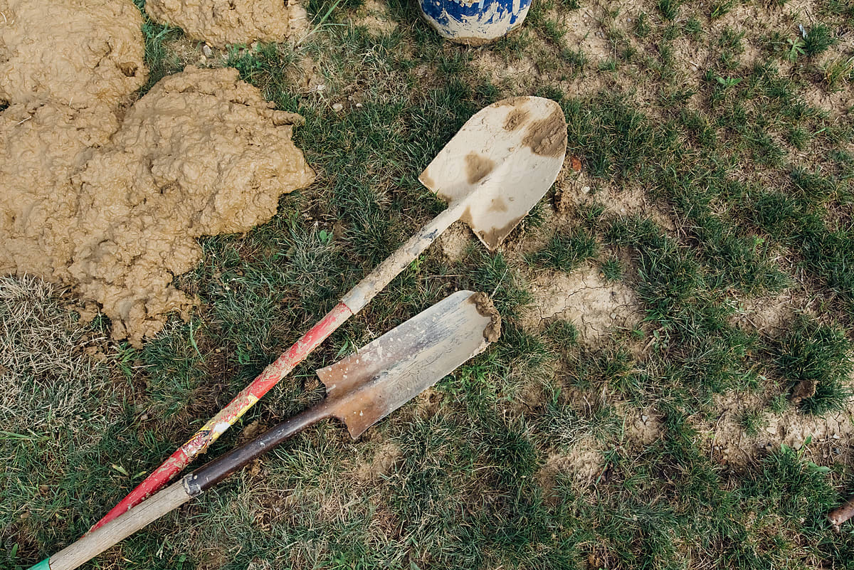 Two mud covered shovels laying on the ground.