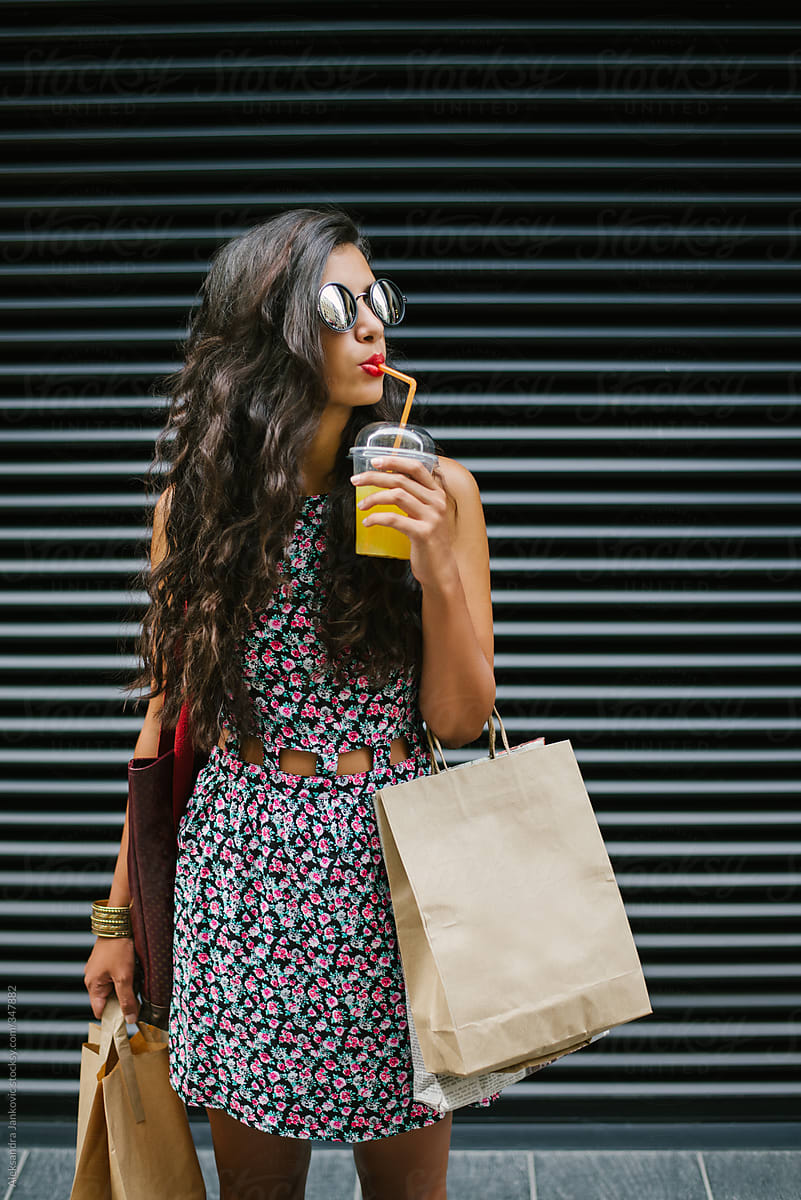 Beautiful Brunette Woman Holding Paper Bags And Drinking Juice On The Street
