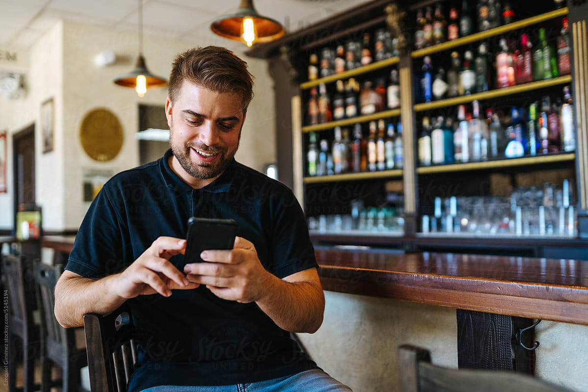 Happy man using smartphone in bar