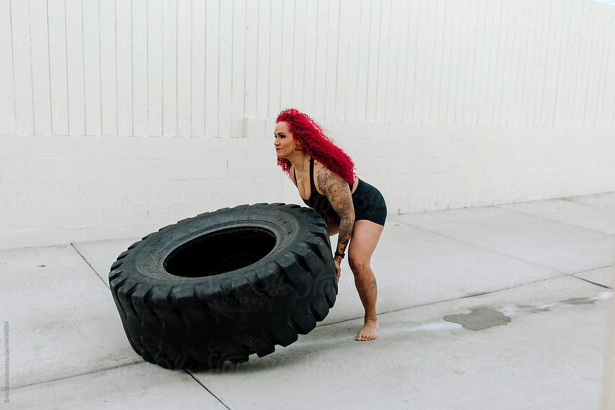 Strong woman with red hair lifting tire