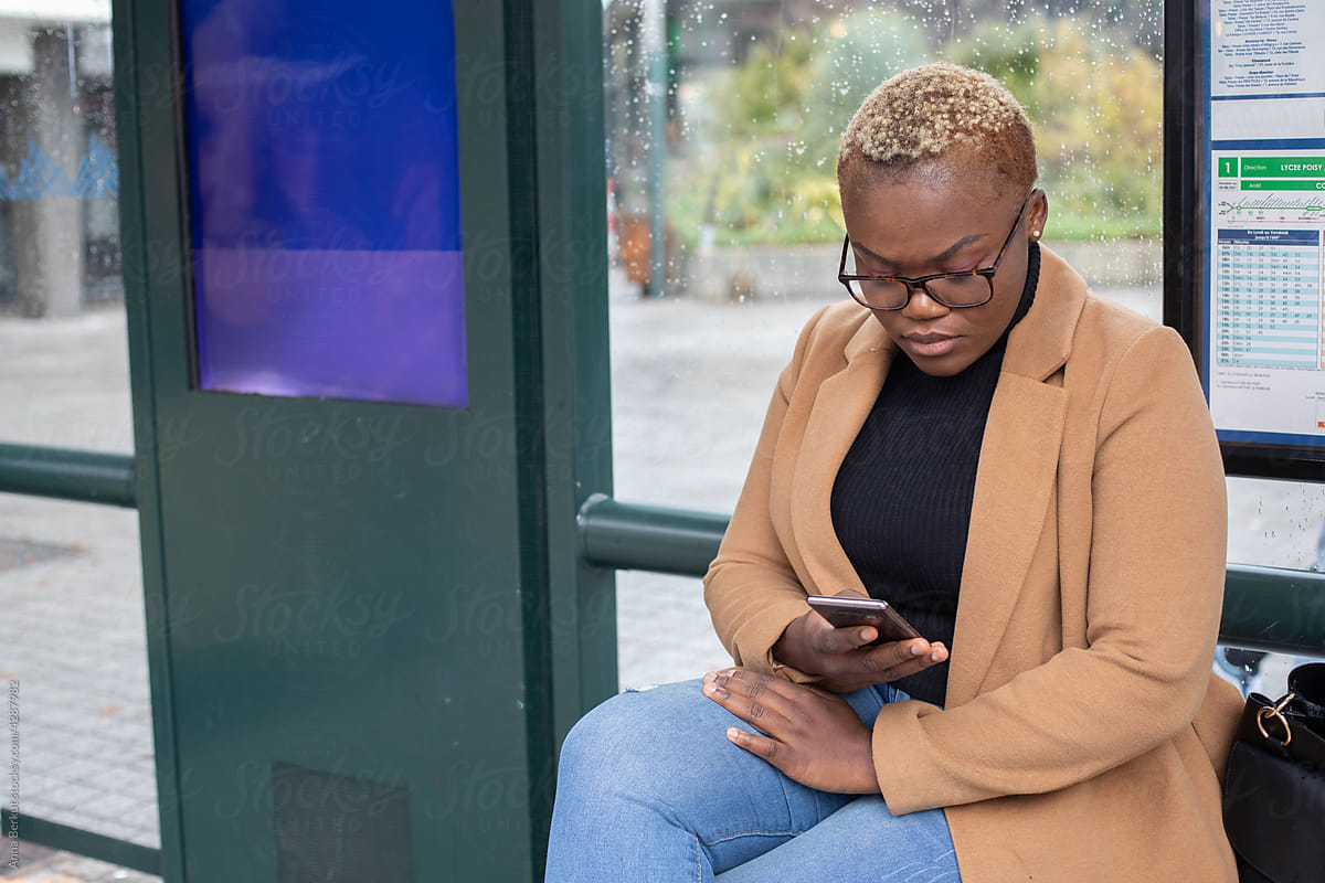 black woman with short hair using smartphone on bus stop, transport