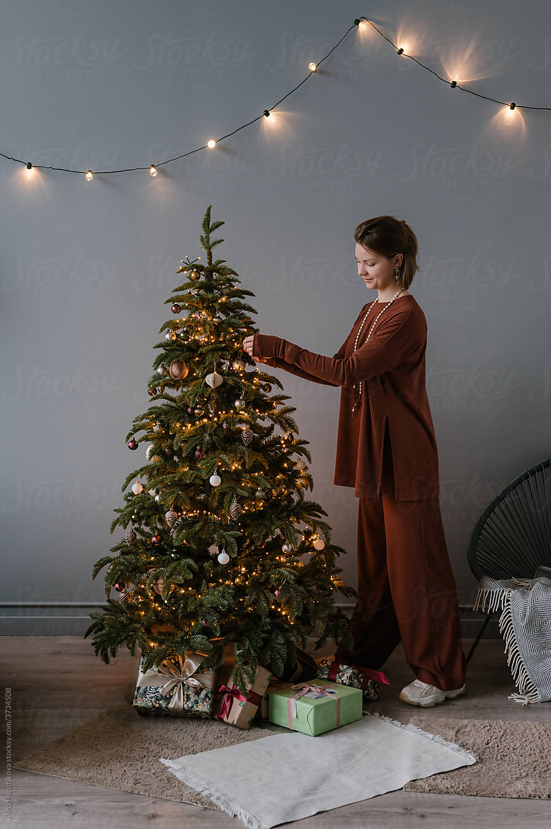 Young female decorating Christmas tree in cozy room